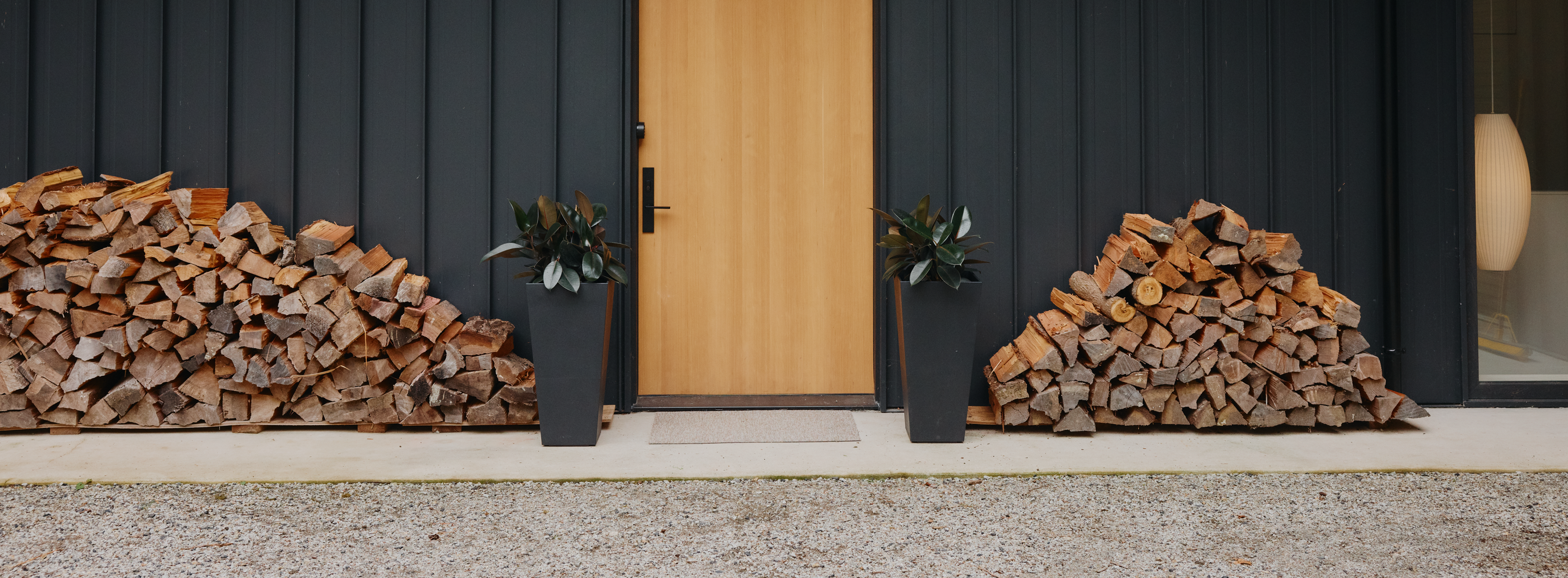 Modern house exterior with black siding, wooden door, and stacked firewood.